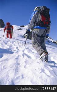 Two mountain climbers walking up snowy mountain (selective focus)