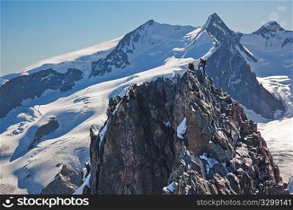 Two mountaneers climb the ridge of Breithorn, exactly on the swiss-italian border. In background the main peaks of Monte Rosa massif (4650 mt, the second highest point in continental Europe) Switzerland, Europe.
