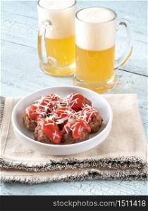 Two mugs of beer with bowl of meatballs