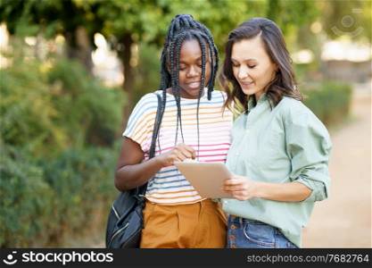 Two multiethnic women consulting something on a digital tablet outdoors.. Two multiethnic women consulting something on a digital tablet.