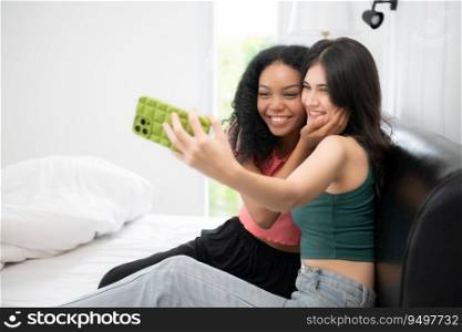 Two multiethnic women taking selfie on mobile phone in bed at home