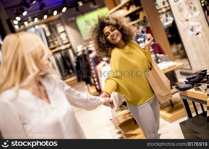 Two multiracial young women choosing clothes from new collection in department store