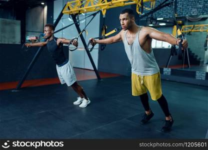Two muscular athletes in sportswear at stretching exercise machine on training in gym. Workout in sport club, healthy lifestyle