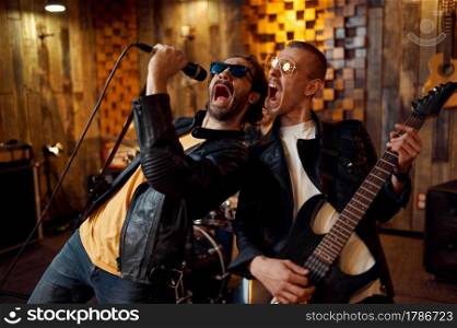 Two musicians at microphone, music performing on stage. Rock band performance or repetition in garage, man with musical instrument, live sound performers. Two musicians at microphone, rock band