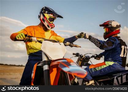 Two MX riders hiting fists for good luck. Greeting, support, wishes of success in competition. Motocross riders hitting fists for good luck