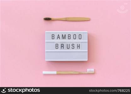 Two natural eco-friendly bamboo brushes with white and black bristles and lightbox text Bamboo brush on paper pink background. Top view Flat lay Template Concept. Two natural eco-friendly bamboo brushes with white and black bristles and lightbox text Bamboo brush on pink paper background. Top view Flat lay Template Concept