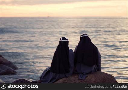 two nuns sitting at the stone on the shore of baltic sea