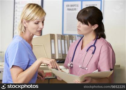 Two Nurses Discussing Patient Notes At Nurses Station