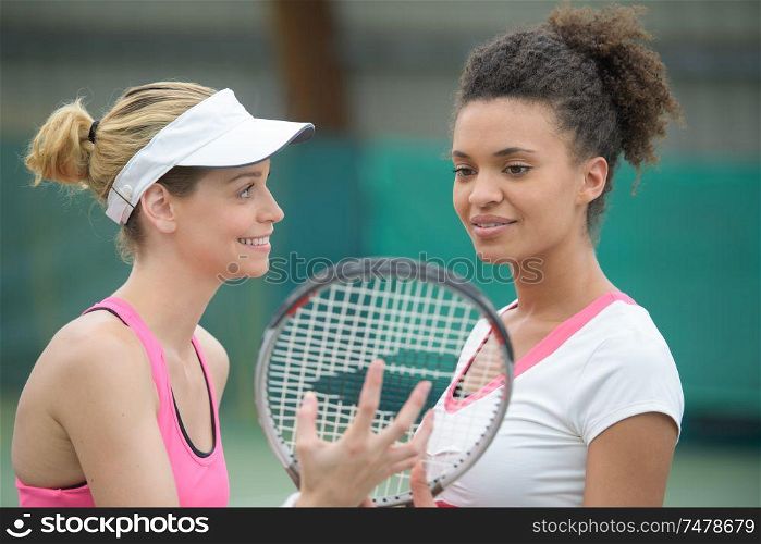 two of attractive smiling female tennis players standing outdoor