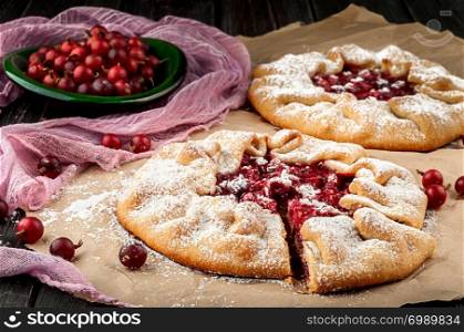 Two of gooseberry galette. Berries of gooseberry on a wooden table and in plate, decorative mesh. The cut out sector of the pie.. Two of gooseberry galette