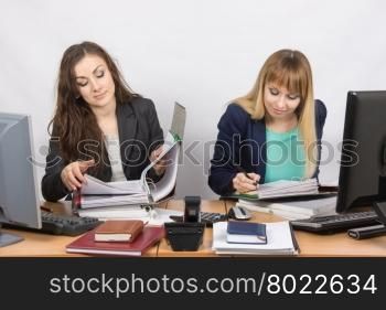 Two office employee sitting at a desk and working with papers and documents