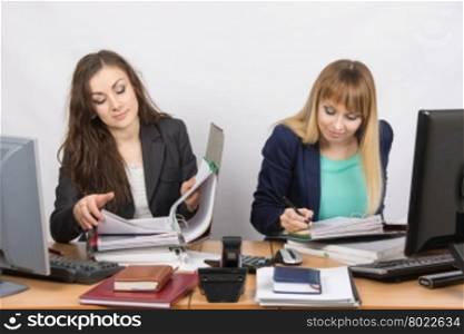 Two office employee sitting at a desk and working with papers and documents