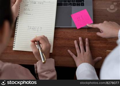 Two office lady colleague collaborating in modern office workspace, engaging in discussion and working together on laptop, writing post note as professional and modern office worker. Enthusiastic. Two young businesswoman work together in office workspace. Enthusiastic