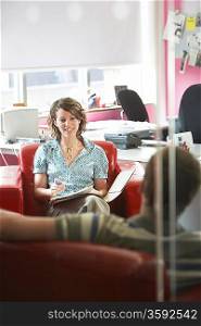 Two office workers sitting on sofas in office elevated view focus on woman