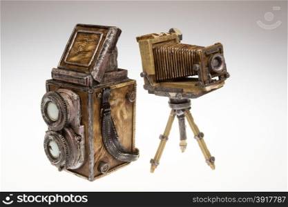 Two old cameras-models for collectors.Two SLR camera lenses and bellows camera on a tripod.Models made of plaster and leather.Cameras on white isolated background.Horizontal view.