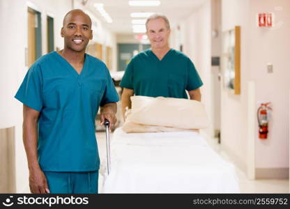 Two Orderlies Pushing An Empty Bed Down A Hospital Corridor