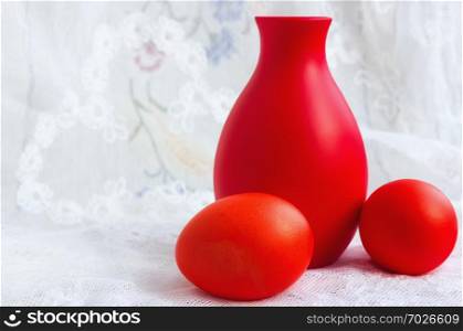 Two painted red Easter eggs and a ceramic jag on a white vintage lace tablecloth. Selective focus on the foreground.. Two Easter Eggs And A Jug On A Lace