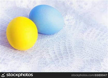 Two painted yellow and blue Easter eggs closeup on a white vintage lace tablecloth. Selective focus, space for copy.. Two Painted Eggs On A Lace
