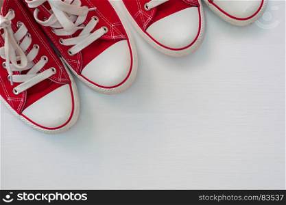 two pair of red sneakers youth on a white wooden surface, empty space