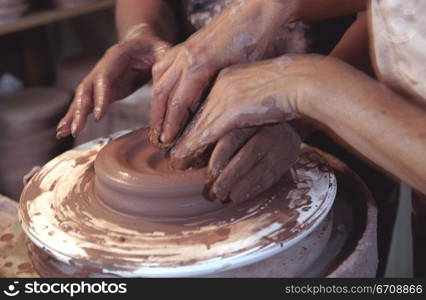 Two pairs of hands shaping clay on a potter&acute;s wheel