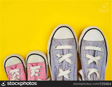 two pairs of worn textile shoes of different sizes on a yellow background, empty space, family concept
