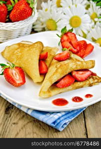 Two pancakes with strawberries and jam on a white plate, basket with berries, bouquet of daisies on a background of wooden boards