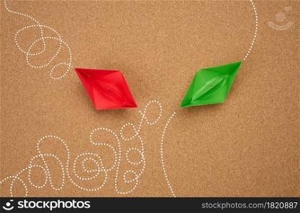 two paper boats with different trajectory on a brown background. The concept of optimal problem solving, achieving goals in different ways, smart and capable employee