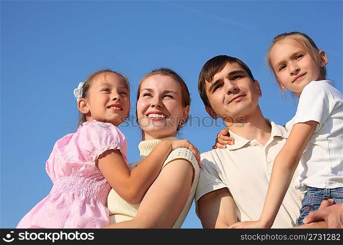 two parents hold children on hands against sky