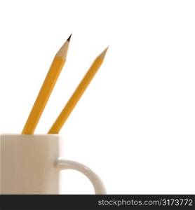 Two pencils in a coffee cup with pointed ends up.