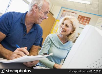 Two people at computer terminal with notepad