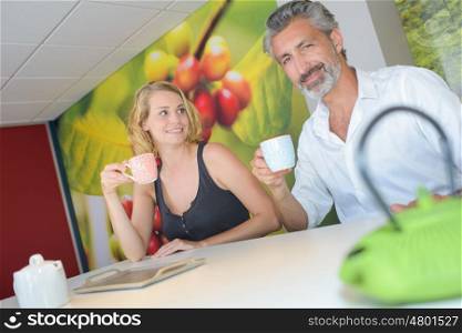 two people at office desk drinking coffee