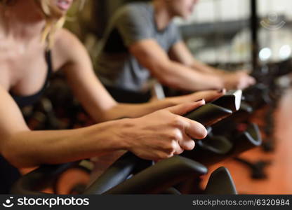 Two people biking in the gym, exercising legs doing cardio workout cycling bikes. Couple in a spinning class wearing sportswear.