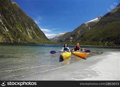 Two people in kayaks near shore of mountain lake