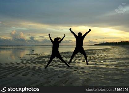 Two people in silhouette jumping happily on a beach