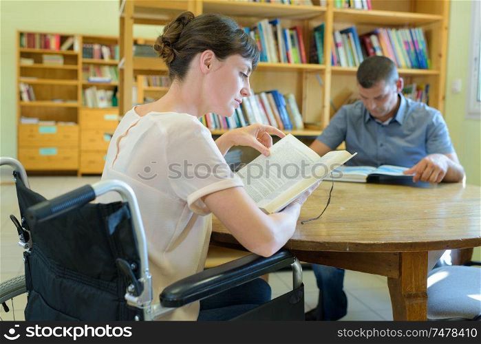 two people reading at table in library woman in wheelchair