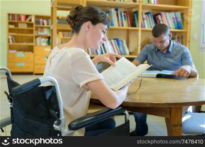 two people reading at table in library woman in wheelchair