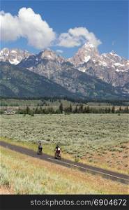 Two people ride along in the forground Rocky Mountains in the background