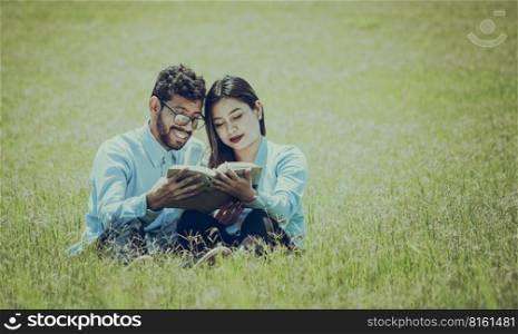 Two people sitting on the grass reading a book, concept of people reading outside, A couple sitting on the grass reading a book