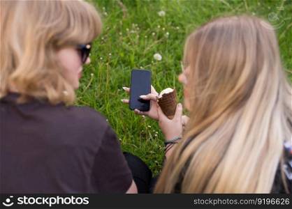 two people, two girls, teenagers, virtual communication, taking a picture, writing a message, outdoor recreation, vacations, mobile phone, girl&rsquo;s hands. A mobile phone in the hands of a cute teenage girl. Ice cream on vacation