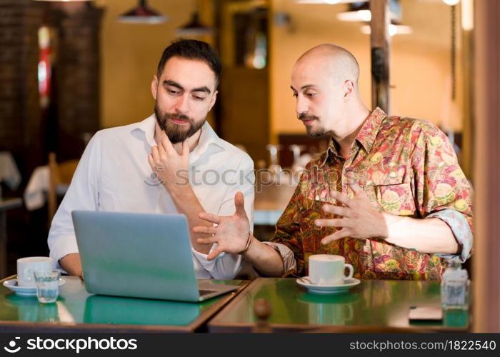 Two people using a laptop together during a meeting at a coffee shop.