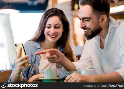 Two people using a mobile phone together while drinking a cup of coffee at a coffee shop.