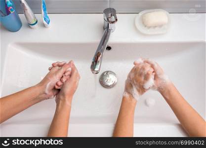 Two people wash their hands in the sink, top view