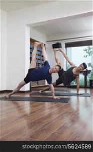 Two people with legs raised and arms outstretched doing yoga in a yoga studio