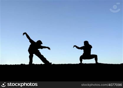 Two persons practicing martial arts on top of a mountain (in silhouette)