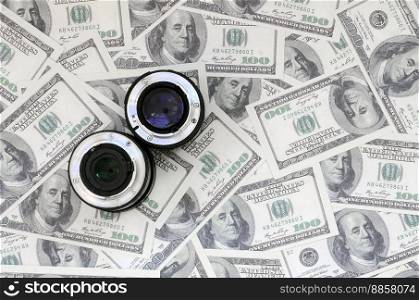 Two photographic lenses lie on the background of a lot of dollar bills. Space for text