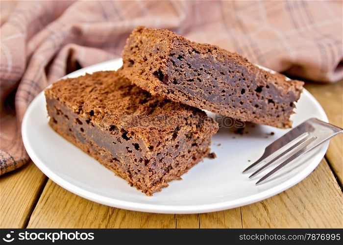 Two pieces of chocolate cake on a plate, fork, napkin on a wooden boards background