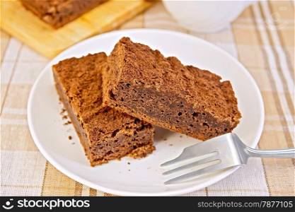 Two pieces of chocolate cake on a plate with a fork on the background of a linen tablecloth