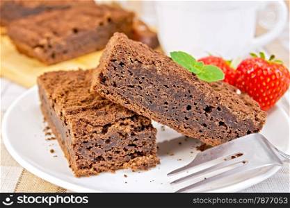 Two pieces of chocolate cake on a plate with strawberries and mint on a fork against a linen tablecloth