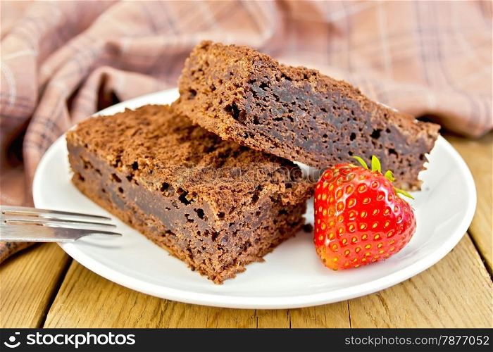 Two pieces of chocolate cake with strawberries on a plate, fork, napkin on a wooden boards background