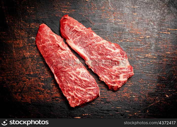 Two pieces of fresh raw steak. On a rustic dark background. High quality photo. Two pieces of fresh raw steak.